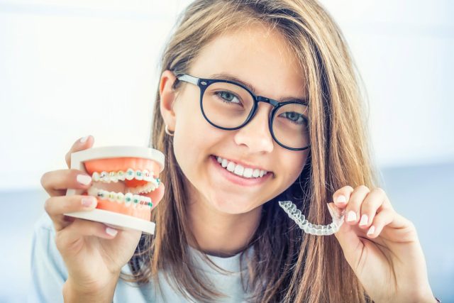 teen girl holding braces and a clear aligner